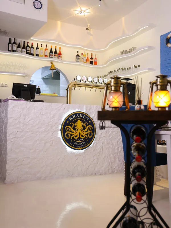The bar: white plaster counter with the gold octopus emblem, wavy shelves of bottles and brass lanterns